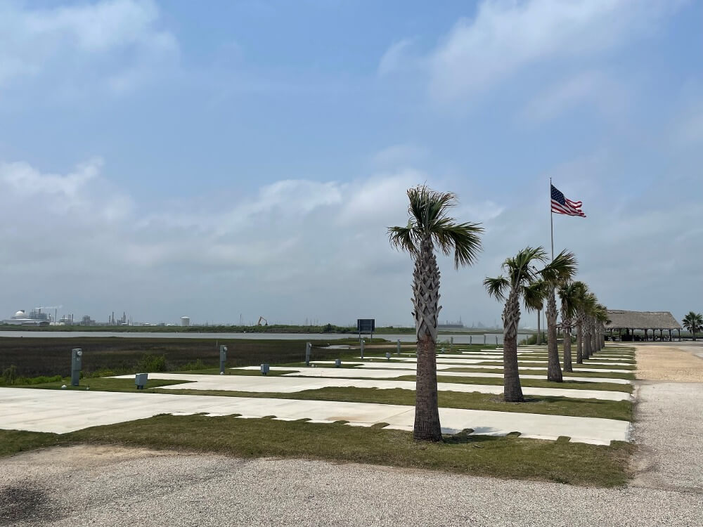 A row of palm trees line the Surfside Marina RV Park. An American flag waves in the background under a partly cloudy sky